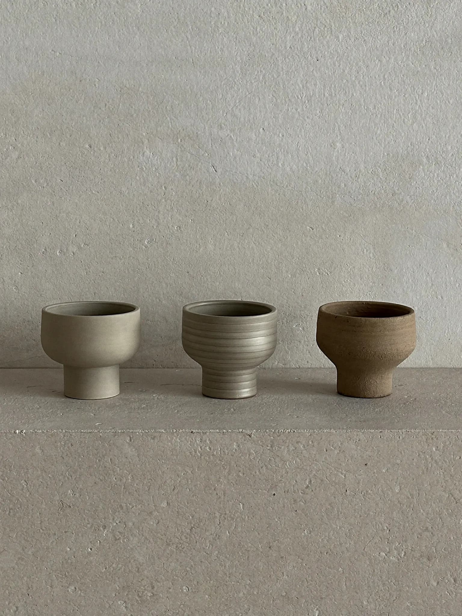 Bud Pots, set of 3 stoneware planter in mixed glaze, on a stone block against a plaster wall