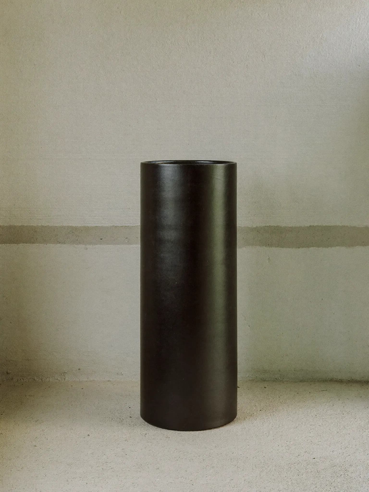 Column stoneware planter in charcoal glaze, on a stone block against a plaster wall