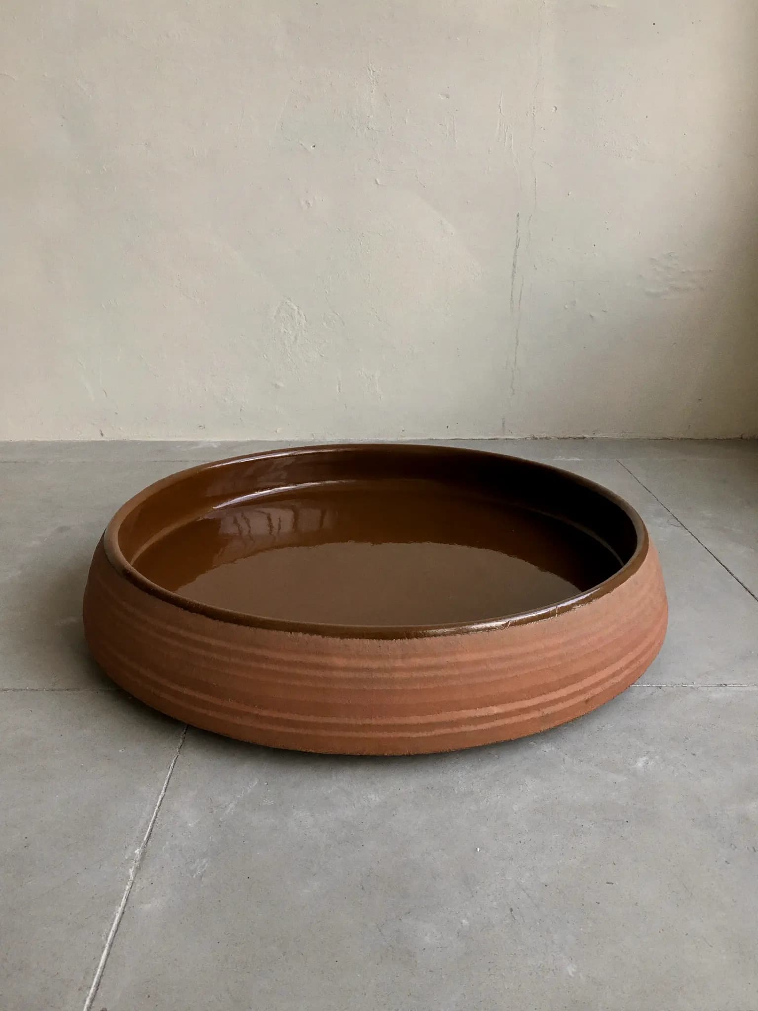 Floor Saucer stoneware piece in raw clay glaze, on a stone block against a plaster wall