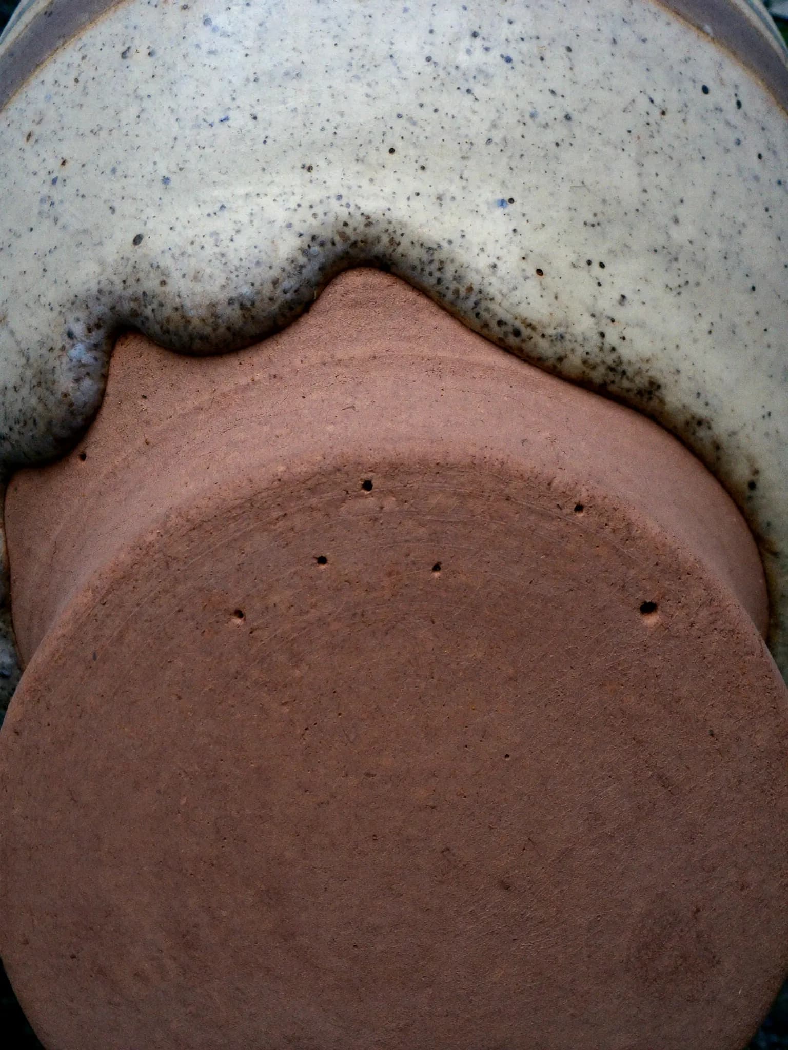 Close-up of speckled cream glaze meeting raw clay at the foot of a pot
