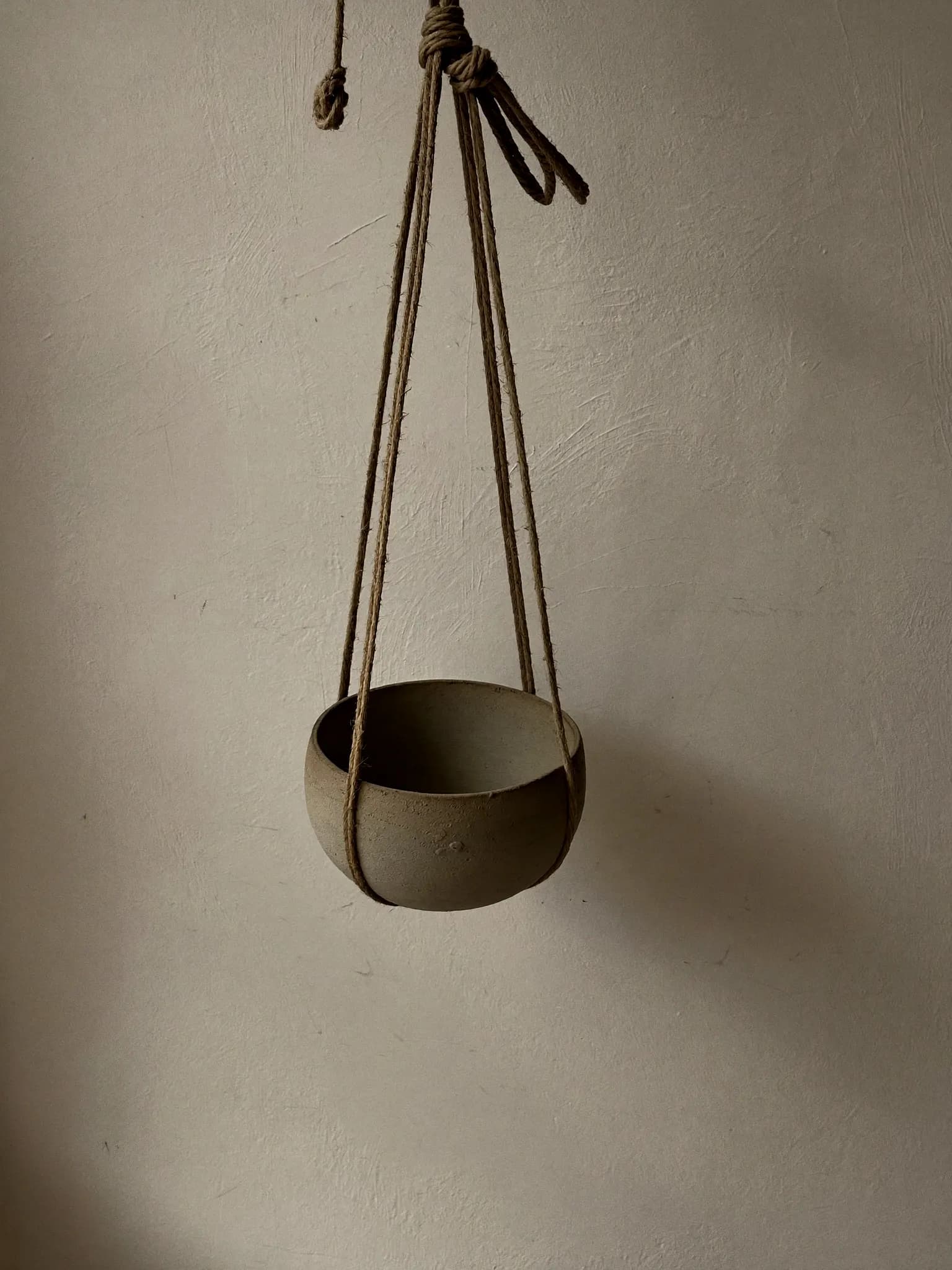 Hanging Bowl stoneware planter in oat matte glaze, on a stone block against a plaster wall