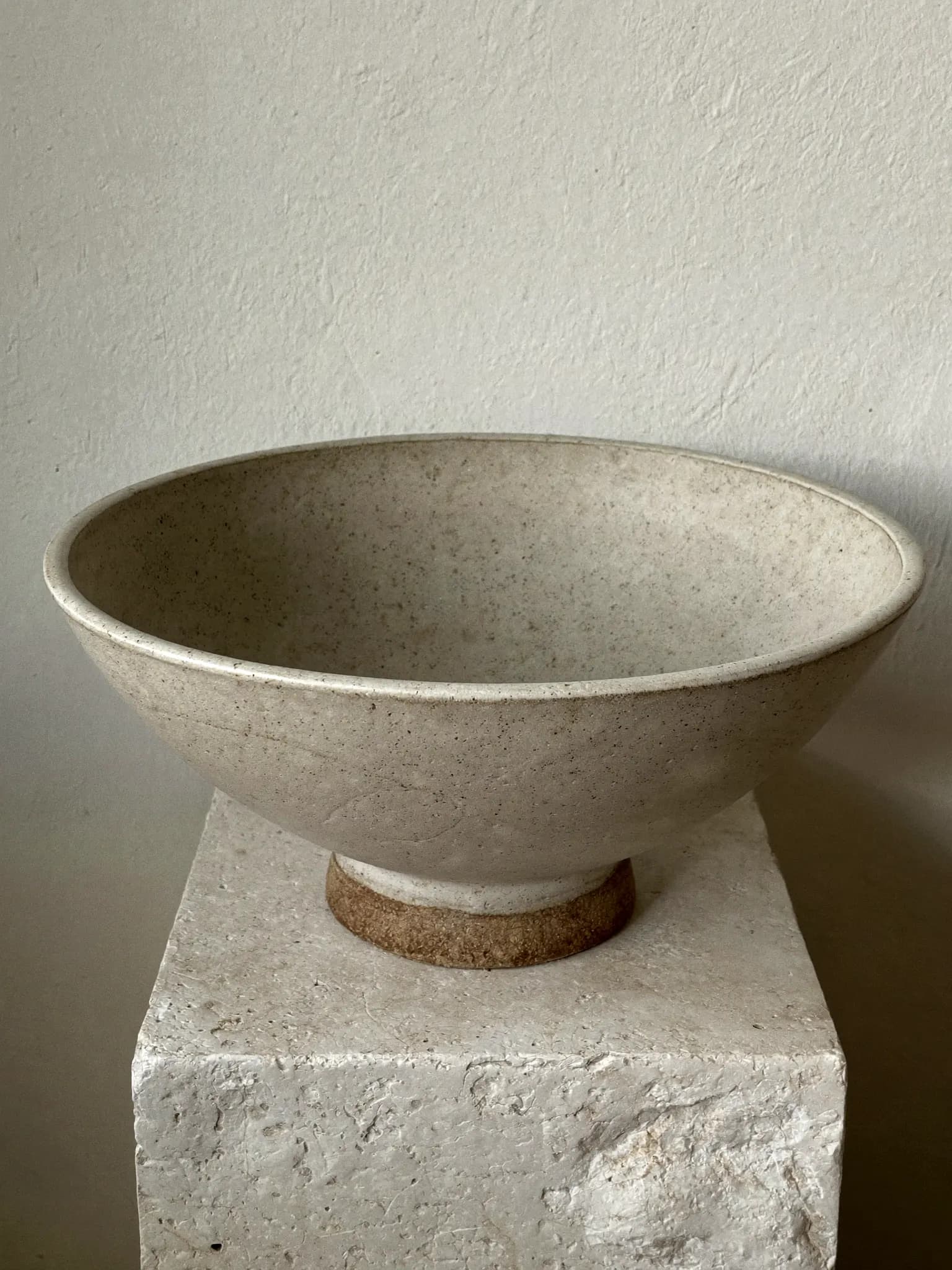 Lowe Bowl stoneware planter in oat matte glaze, on a stone block against a plaster wall