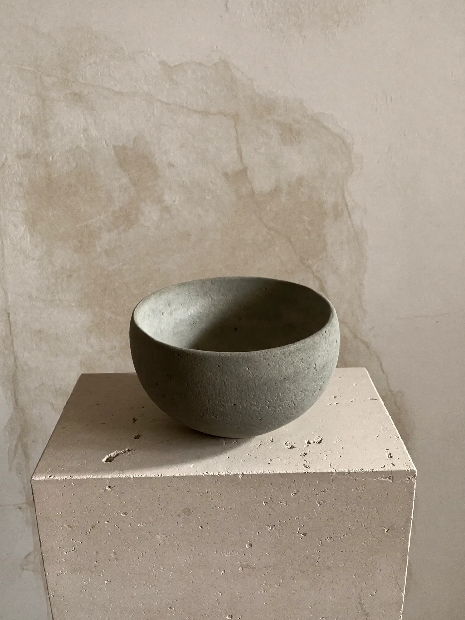 Pebble Pot stoneware planter in ash grey glaze, on a stone block against a plaster wall