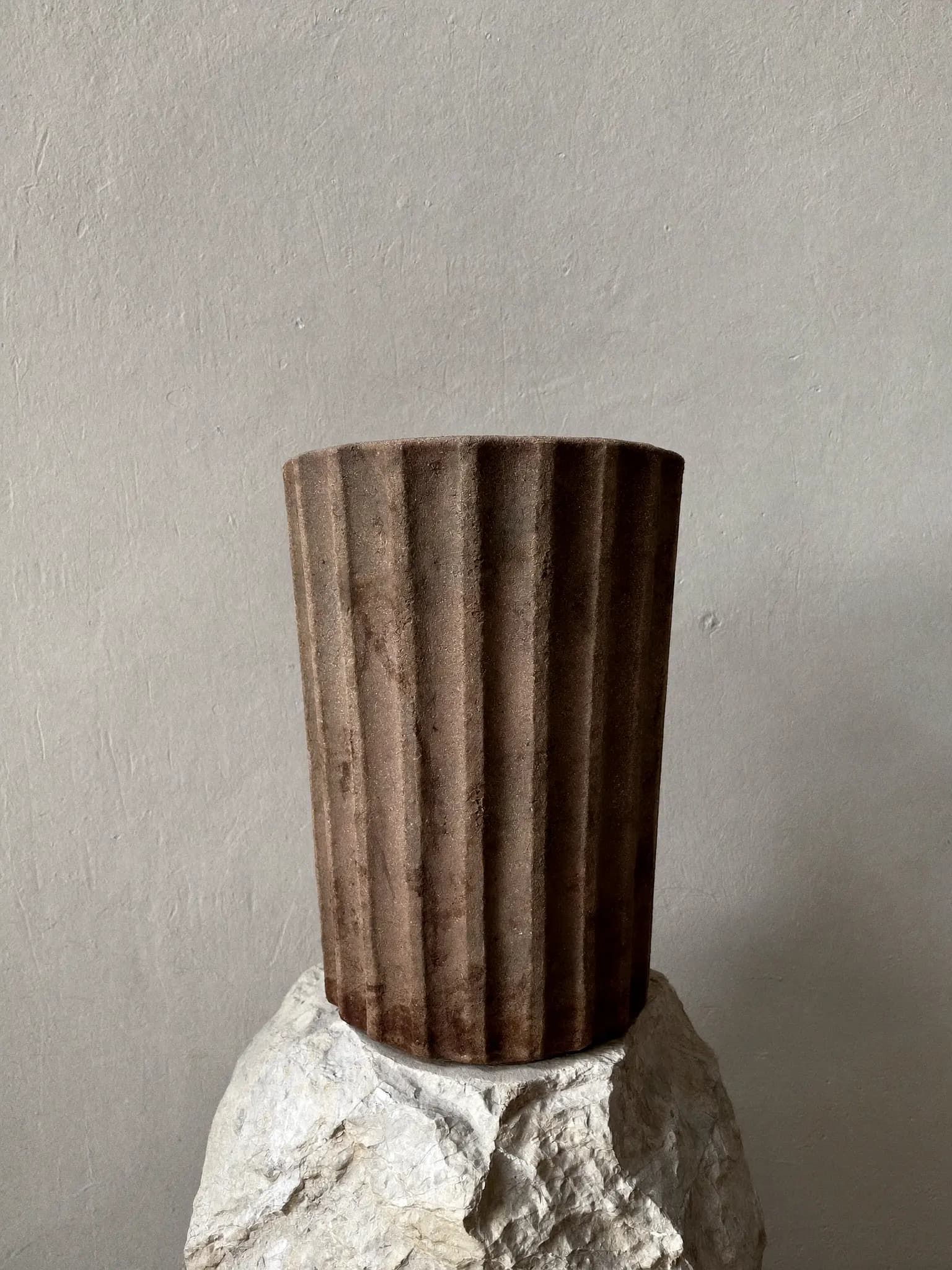 Ridge Cylinder stoneware planter in raw clay glaze, on a stone block against a plaster wall