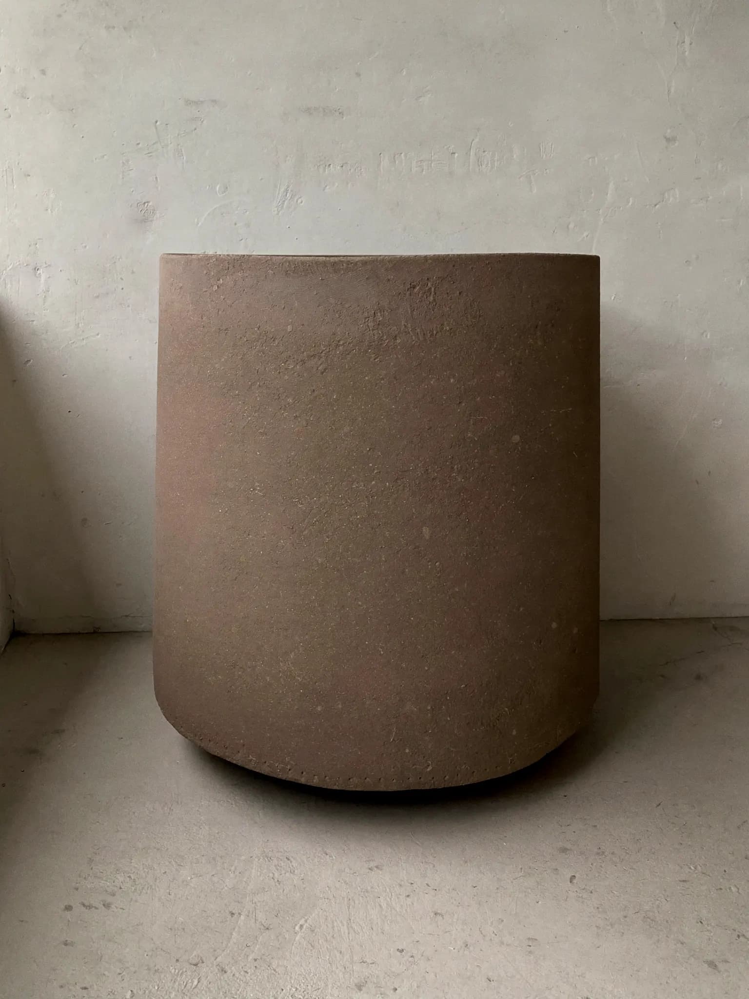 Stand Pot stoneware planter in raw clay glaze, on a stone block against a plaster wall