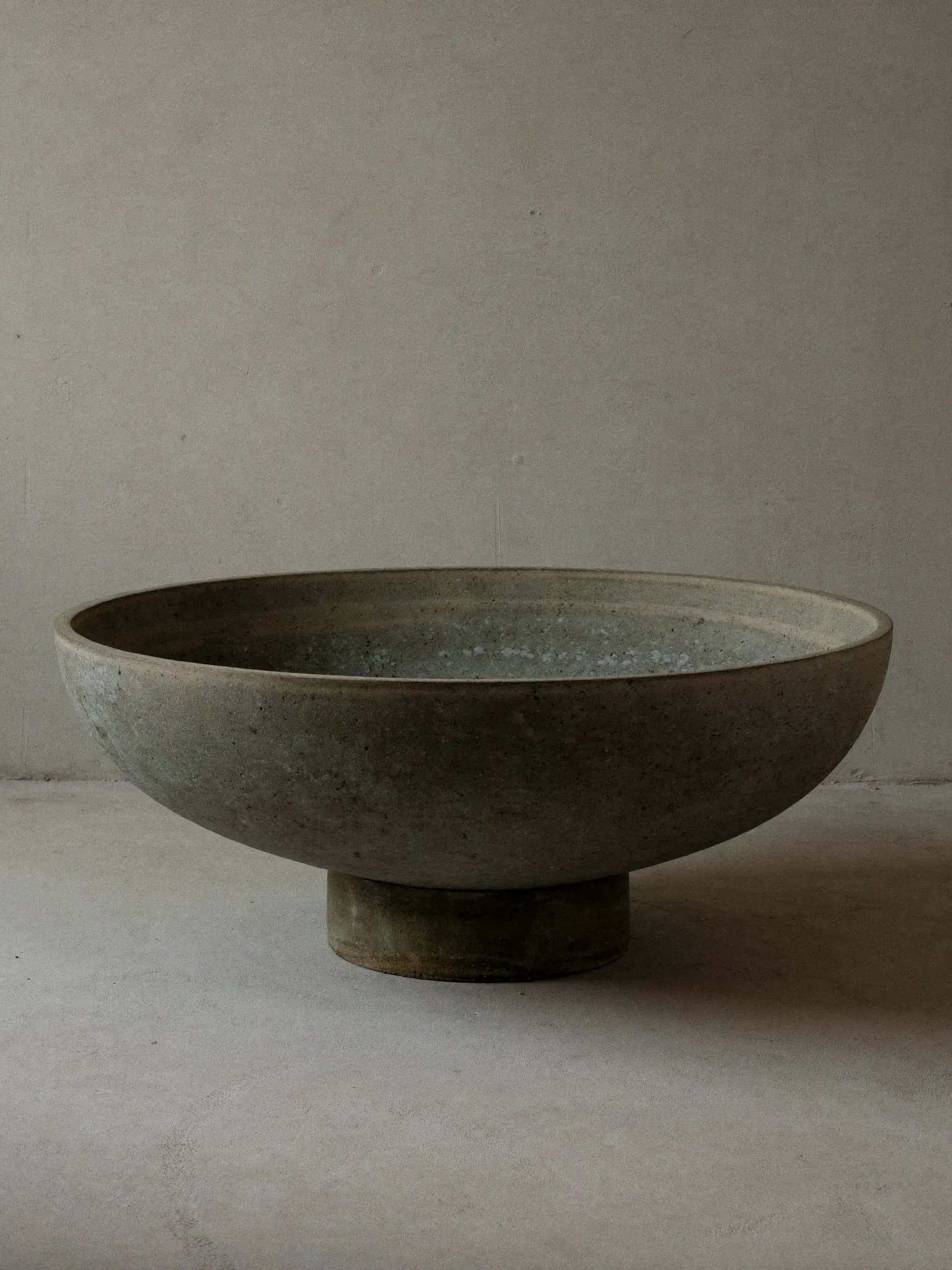 Wide Basin stoneware planter in ash grey glaze, on a stone block against a plaster wall